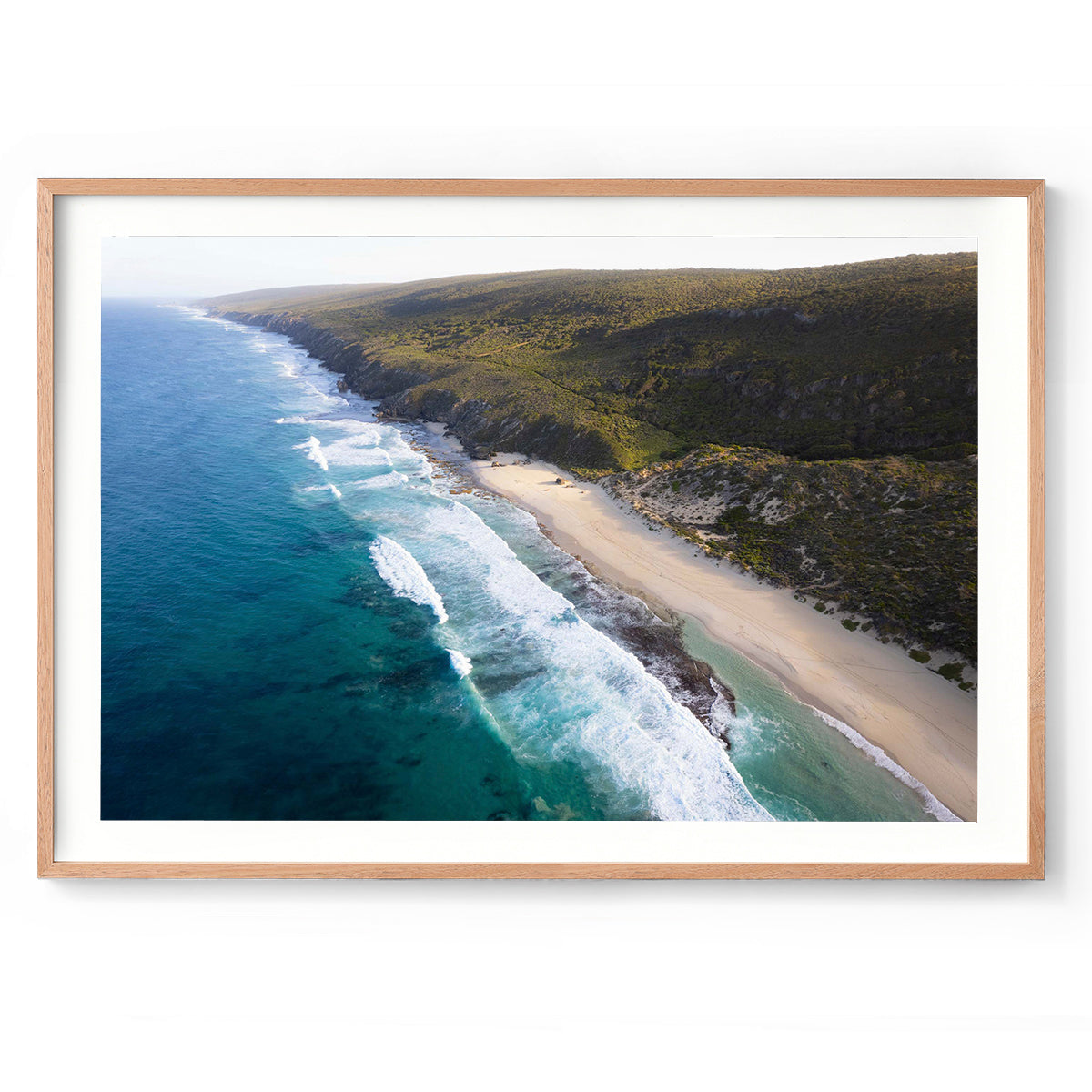 Horizontal drone photo of the far end of Yallingup Beach with the waves rolling in to the white sand and the bushland stretching into the distance. Original fine art photography of Western Australia, available as prints and framed wall art. Perfect for a coastal home or beach house.