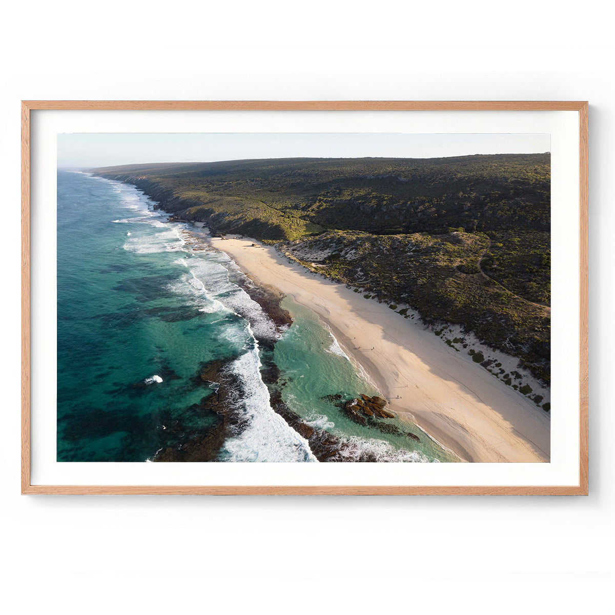 Horizontal drone photo of the far end of Yallingup Beach with the waves rolling in to the white sand and the bushland stretching into the distance. Original fine art photography of Western Australia, available as prints and framed wall art. Perfect for a coastal home or beach house.