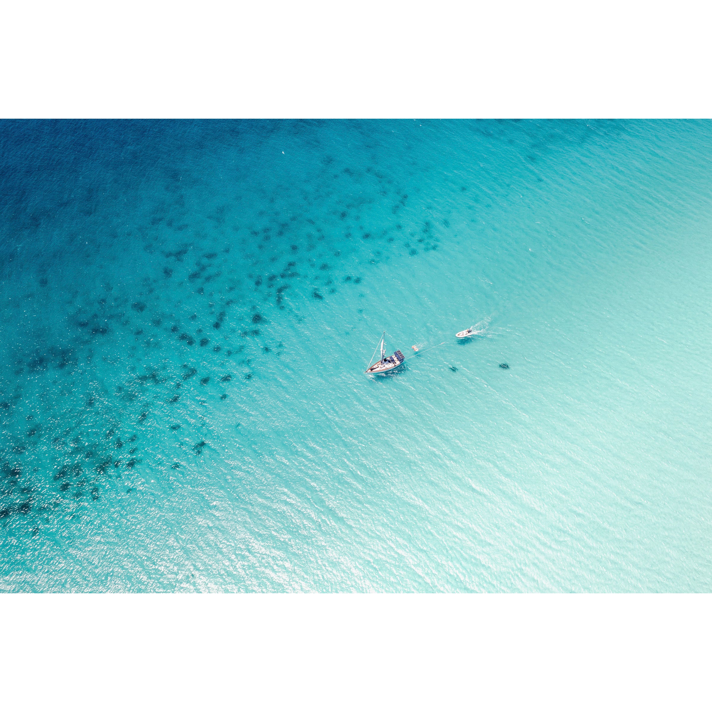 Horizontal drone photo taken at Eagle Bay in Western Australia, the ocean is blue and sparkling and there is a singular boat floating through the water. Minimalist fine art photography for coastal interiors and beach homes. Original framed wall art, exclusive to Host Studio.
