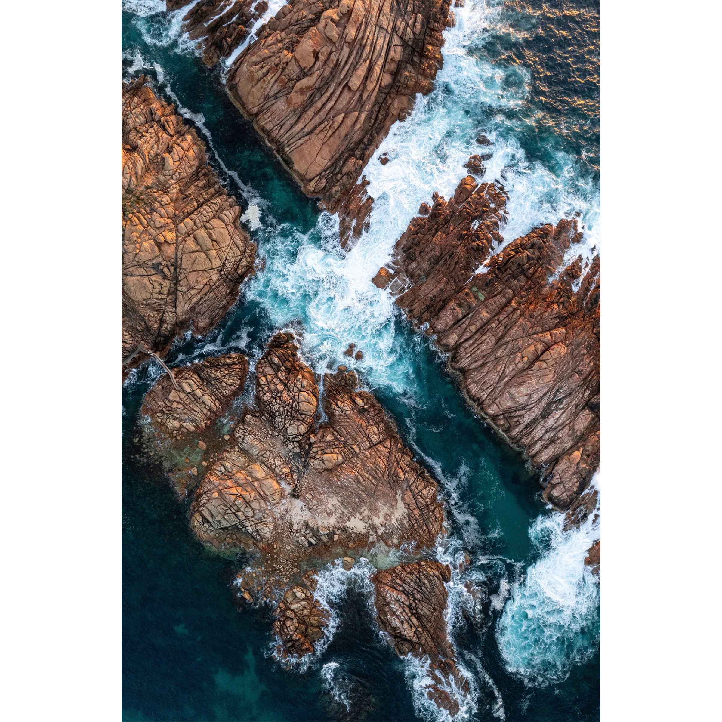 Vertical aerial photo of Canal Rocks in Western Australia near Yallingup. The deep blue ocean is crashing against the rocks creating whitewash that swirls around them. There is a tiny bridge leading from one rock to another on the left hand side. Original fine art photography, available as prints and framed wall art. Perfect for your living room, dining room, bedroom or home office. Shipped free worldwide.