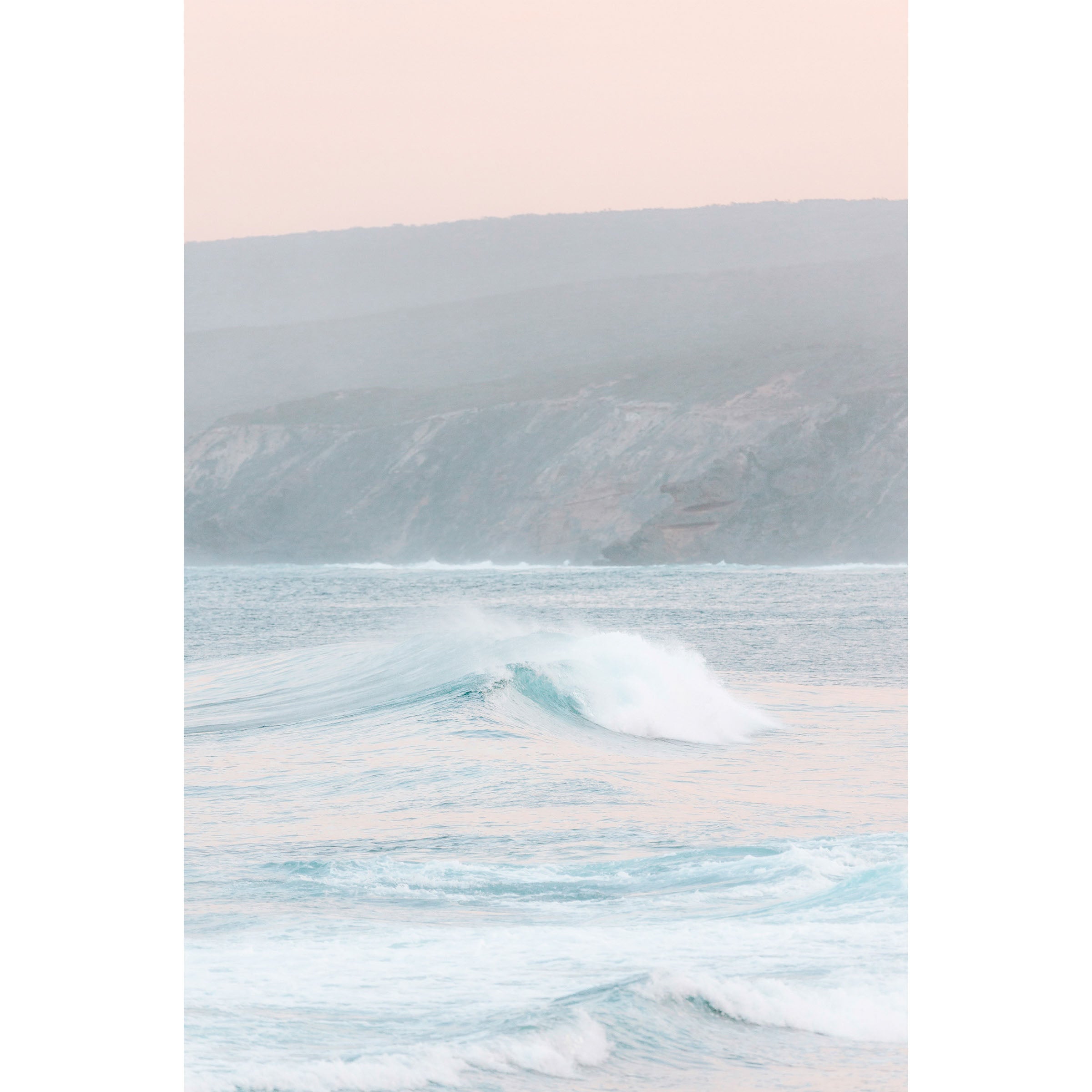 Vertical photo of a pastel sunrise over Yallingup Beach in Western Australia. The colours are soft with the waves rolling in and the cliffs in the background. Available framed in black, white and oak.