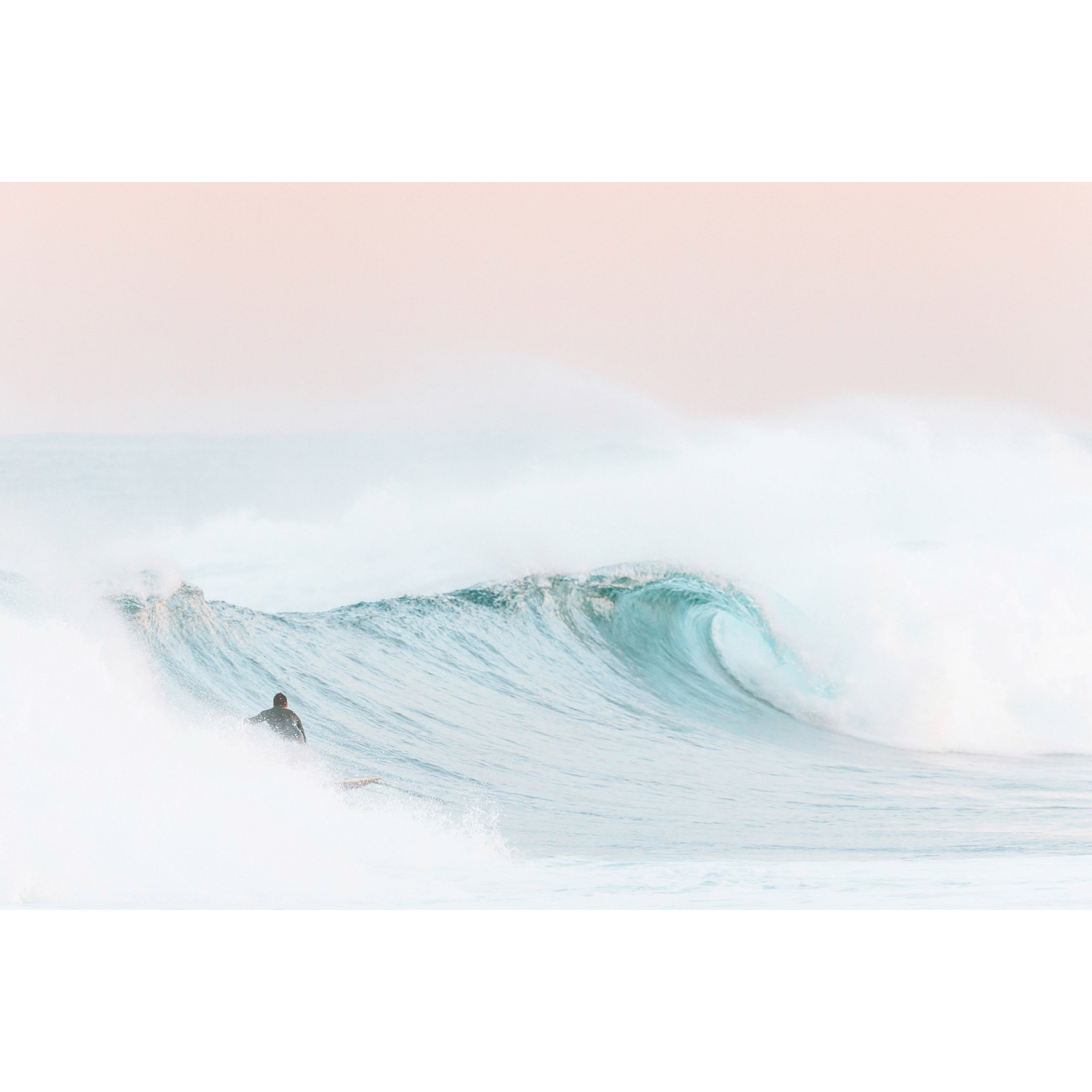 Framed photo of a surfer on a light blue wave with a pink sky at sunrise at Yallingup Beach in Western Australia. Available framed in oak, black or white.