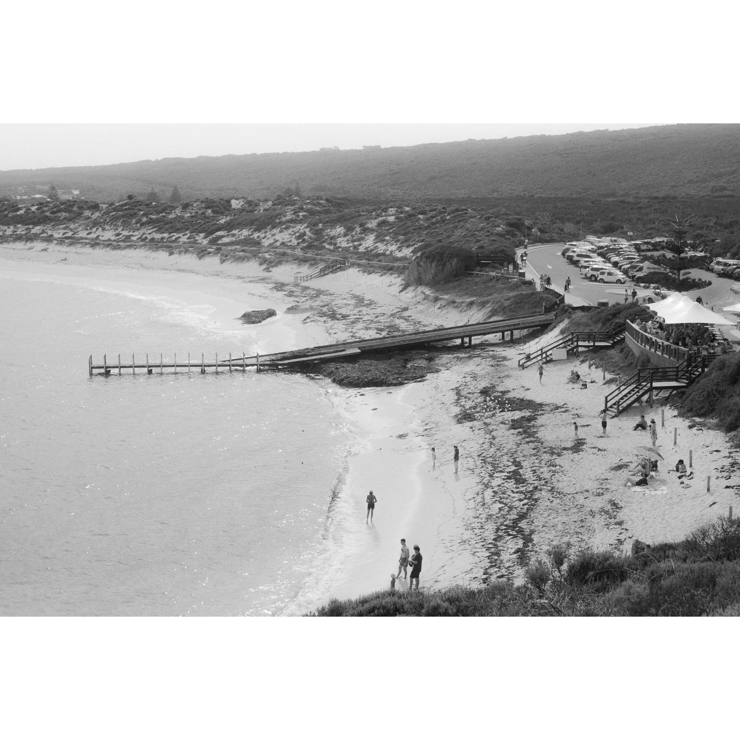 Black and white photo of Gnarabup beach in Margaret River, Western Australia. It shows the jetty and White Elephant Cafe and people on the sand, it has a nostalgic feel to it - shot on film.