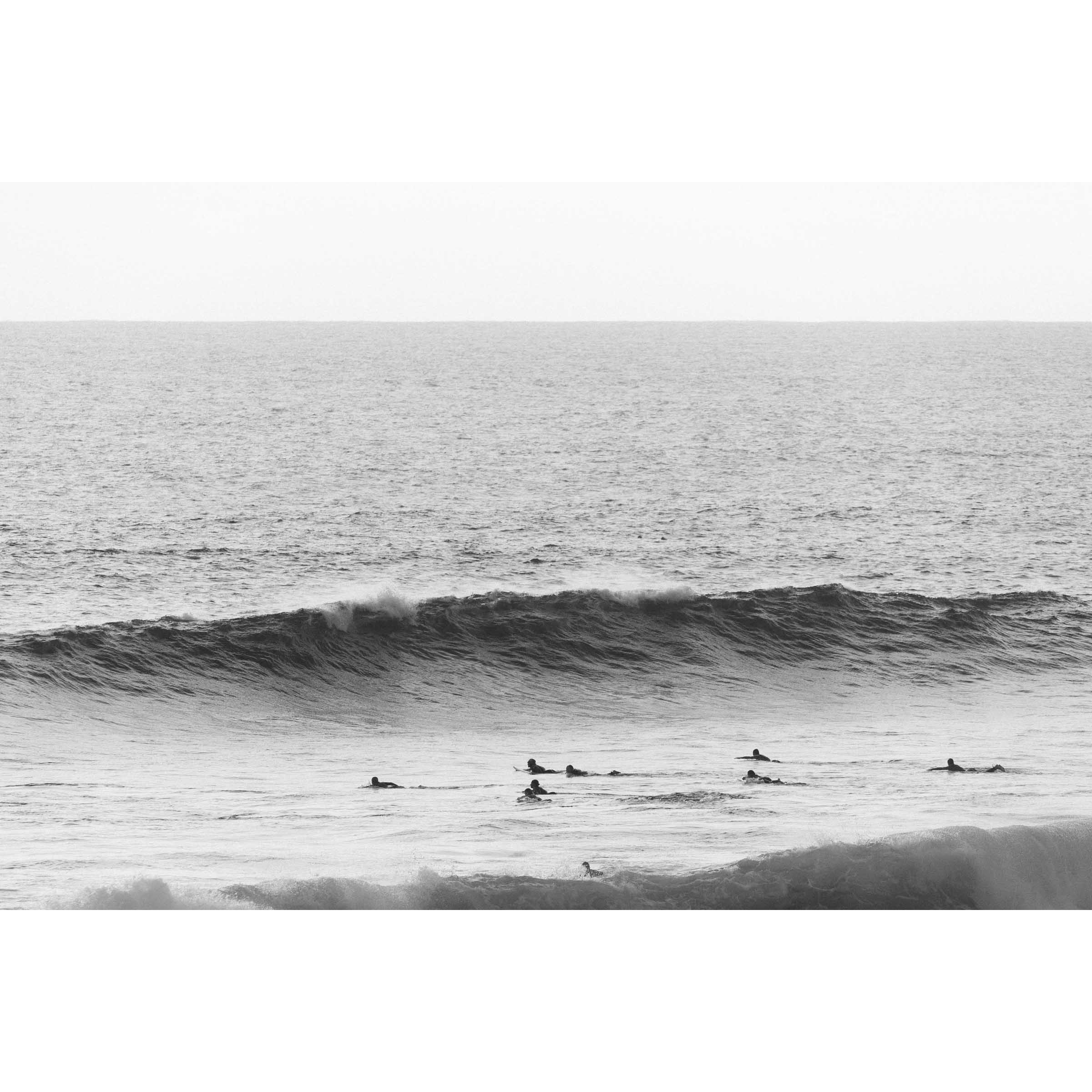 Minimalist black and white photo of surfers paddling out towards a wave in the ocean at Yallingup Beach, Western Australia. Fine art photography prints, available framed in black, white or oak.