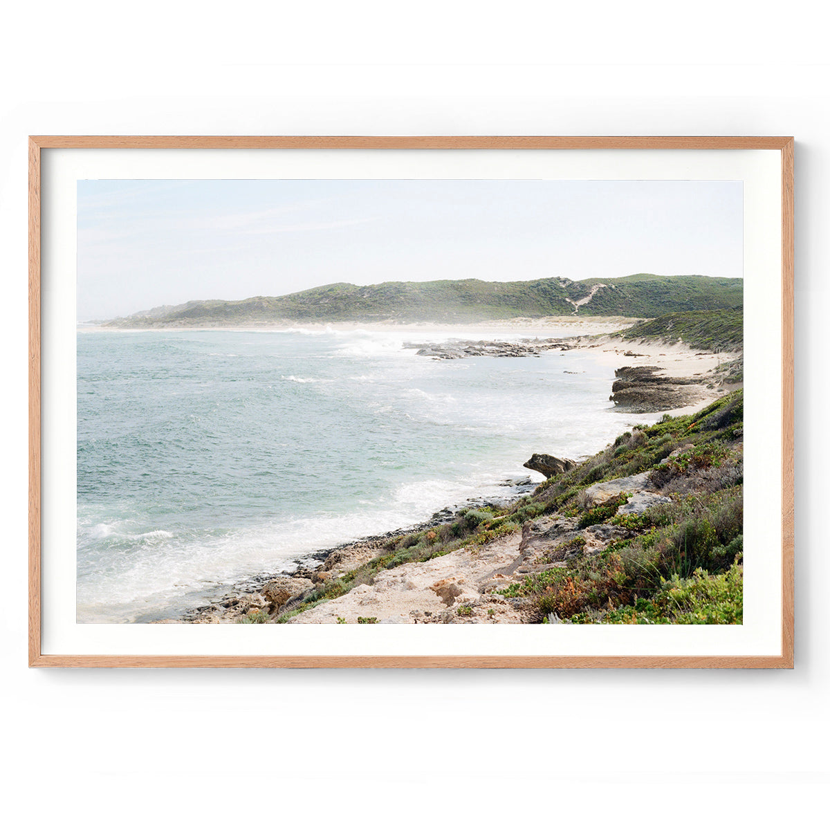 Photo of a coastal landscape at Surfer's Point in Margaret River, Western Australia. Soft ocean waves roll in with the bush and rocks curving around. The spray from the ocean makes it a bit dreamy, as well as soft colours as it's shot on film. Available framed in black, white or oak.