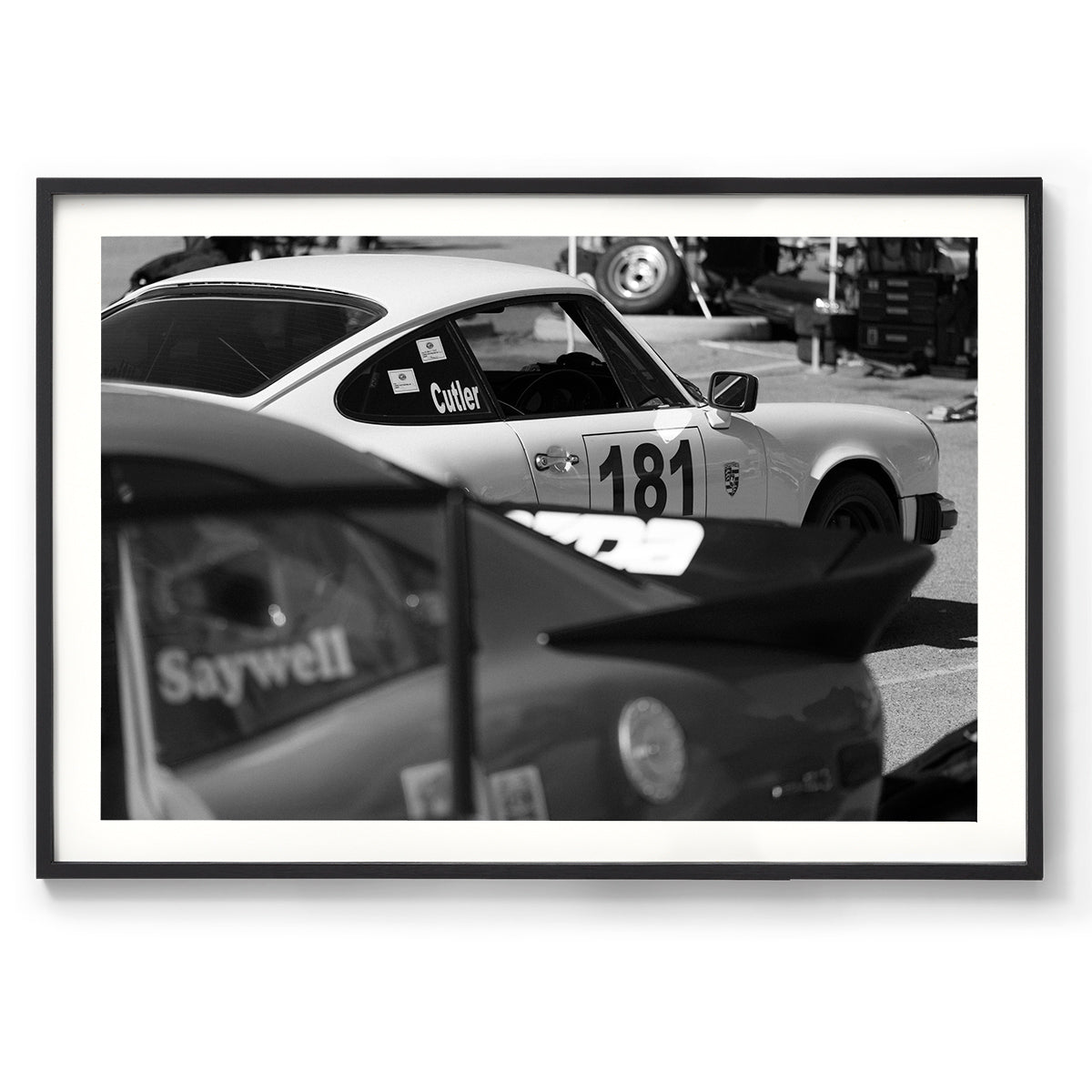 Horizontal black and white photo of a Porsche 911 with a race number on the side waiting in the pits to race again. Fine art photography prints, available framed in black, white or oak.
