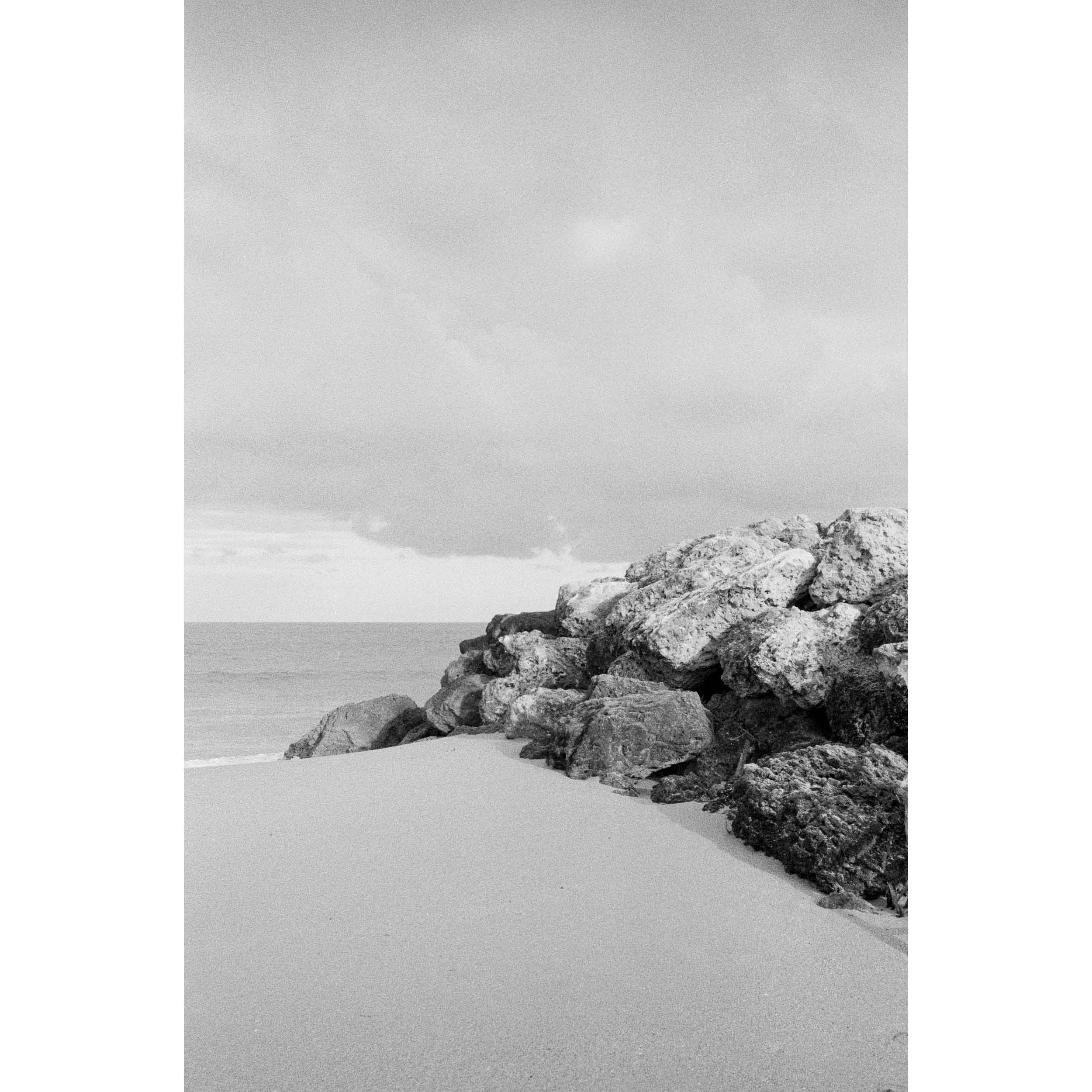 Vertical black and white photo shot on film of some rocks looking out towards the ocean at a beach in Western Australia. Very minimalist and soft. Perfect for a luxury coastal interior or beach house. Available as framed wall art or unframed prints.