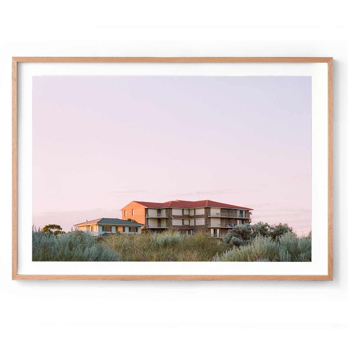 Horizontal photo of the top of a brick 80s block of units in Mandurah, Western Australia. Most of the photo is a soft, lavender sky with silver green bushes in the foreground. Original fine art photography, available as prints and framed wall art.
