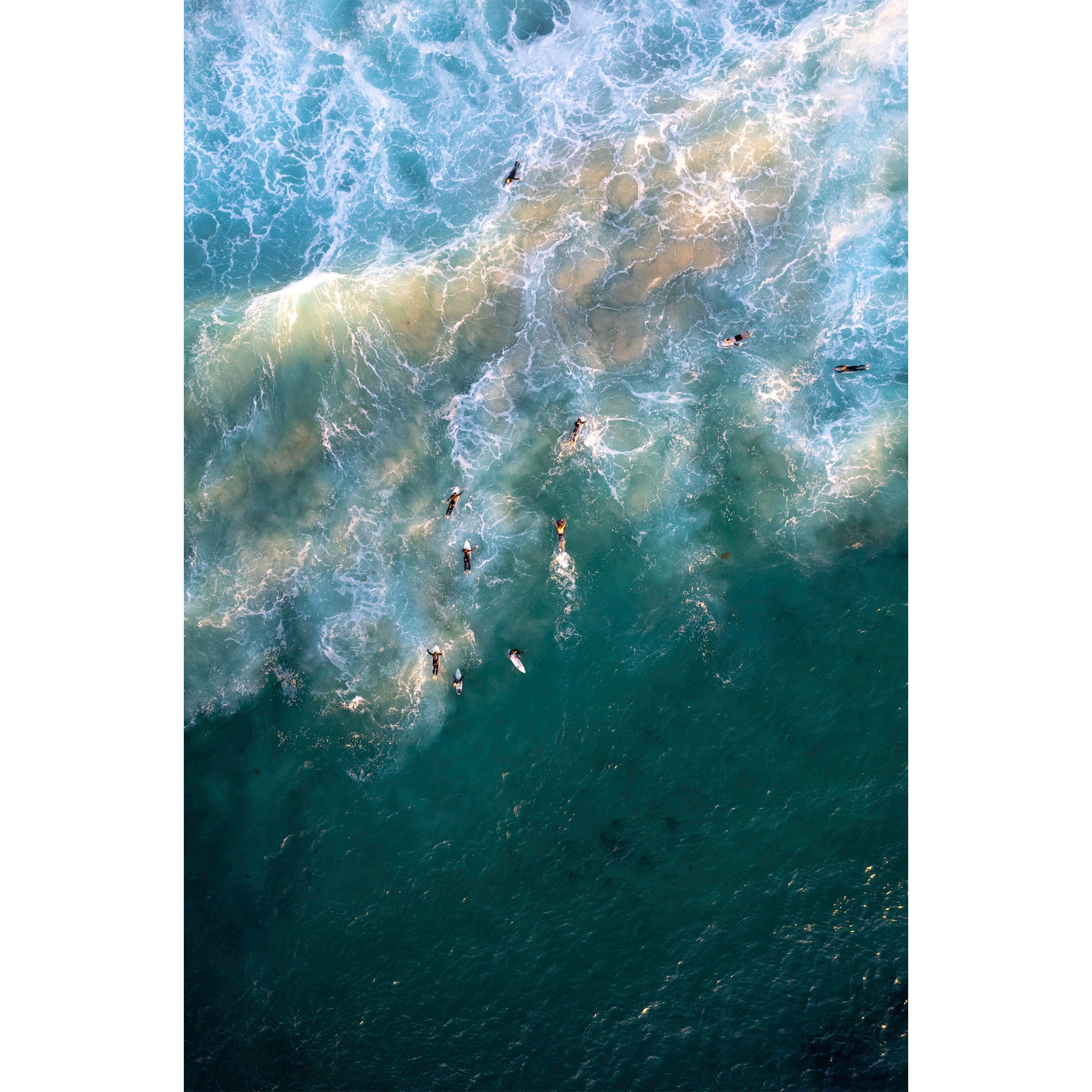 Vertical aerial photo of surfers in the water at sunset at Yallingup beach, Western Australia. The swell is lit up by the golden sunlight as the surfers are dotted through the water. Perfect for a coastal home or beach house. Original fine art photography, available as prints and framed wall art.