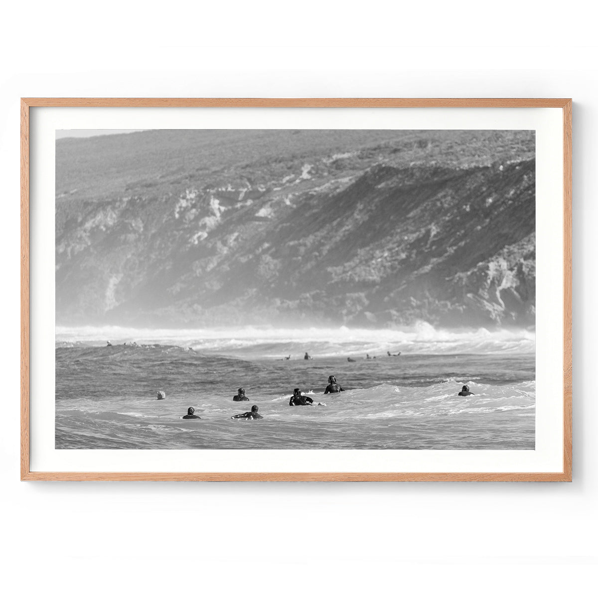 Black and white photo of surfers paddling in the ocean at Yallingup Beach with Rabbit Hill in the background. Fine art photography print from Western Australia's south west, available framed in black, white or oak.