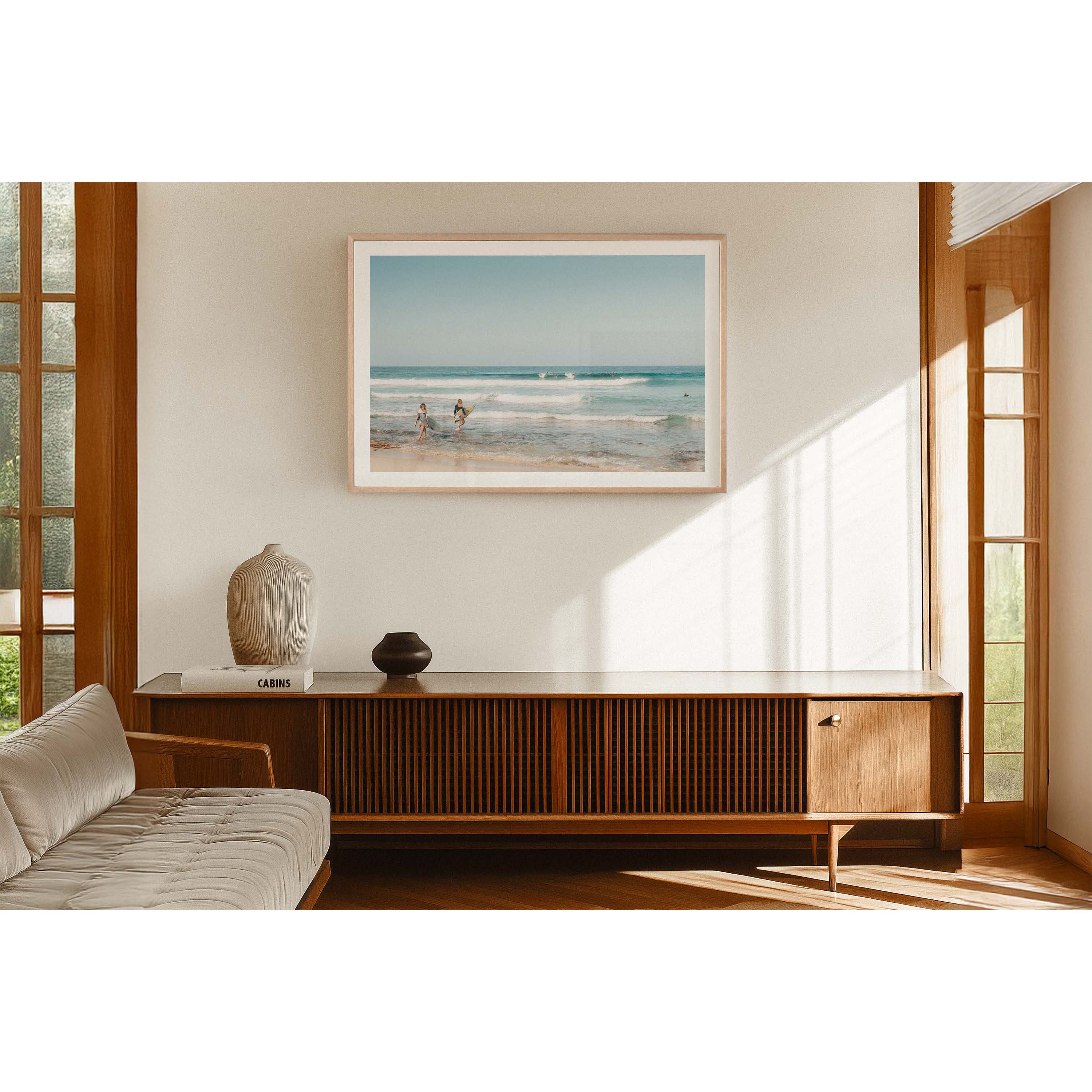 Framed horizontal photo of two female surfers walking into the ocean at Yallingup Beach in Western Australia holding their surfboards under their arms. Waves are rolling in with surfers dotted throughout the soft blue water. Available framed in oak, black or white.