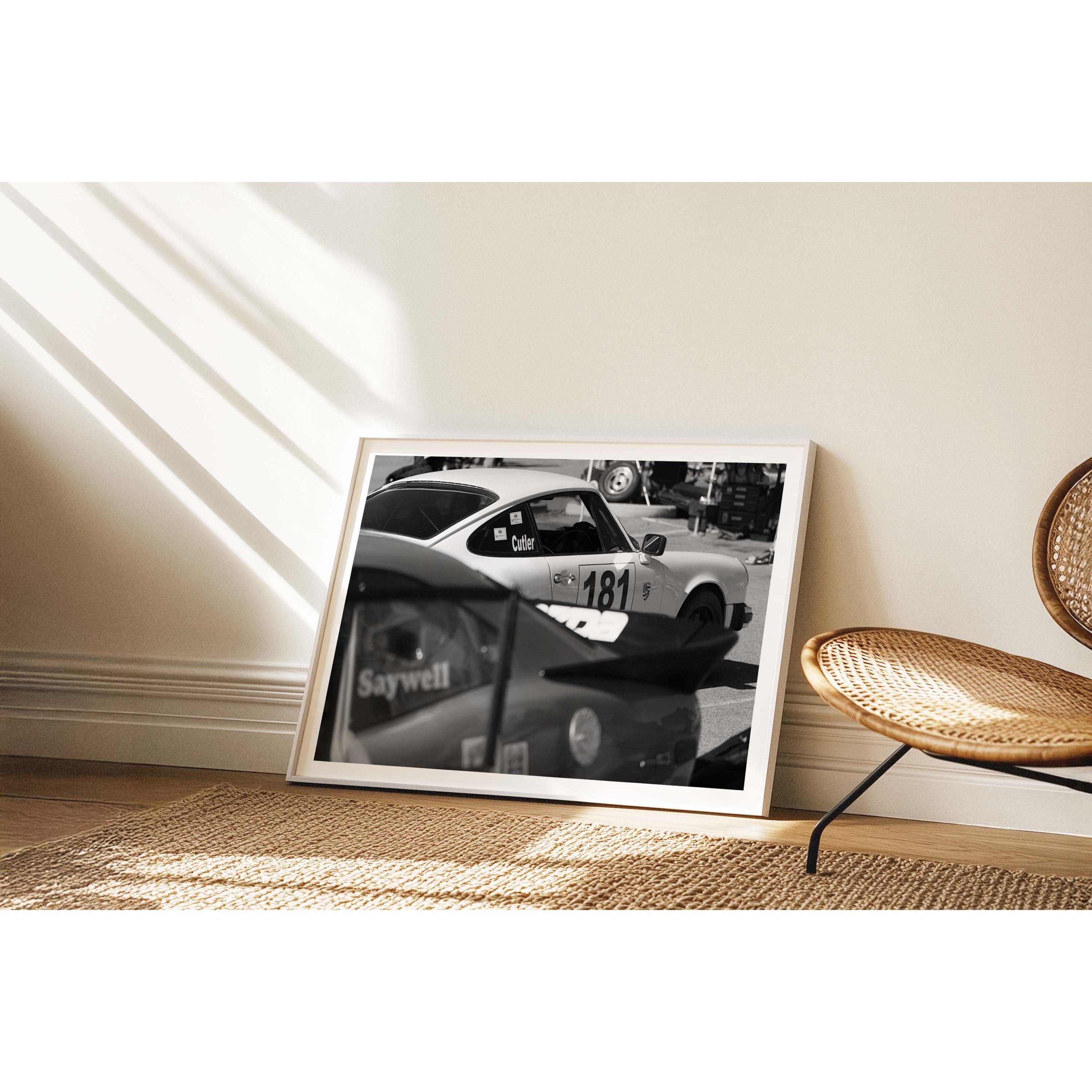 Horizontal black and white photo of a Porsche 911 with a race number on the side waiting in the pits to race again. Fine art photography prints, available framed in black, white or oak.