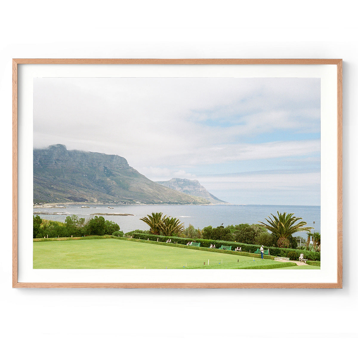 Horizontal framed photo of a bowling green overlooking the ocean in Cape Town, South Africa with the mountains in the background. Shot on film with soft colours. Fine art photography prints, available framed in oak, black or white.