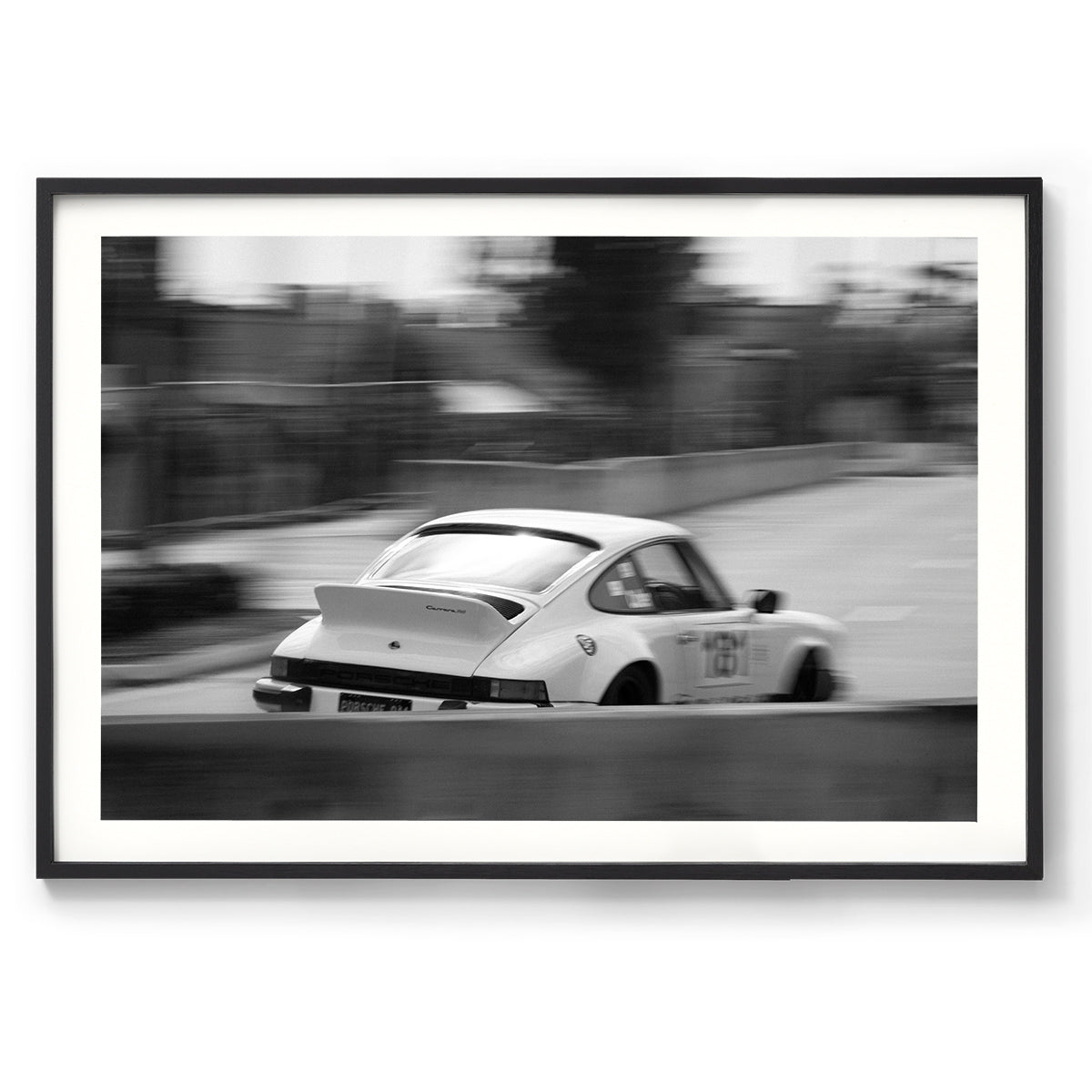 Horizontal black and white photo of a white Porsche 911 racing in the streets, the background is blurred as it goes around a corner. Fine art photography prints, available framed in black, white or oak.