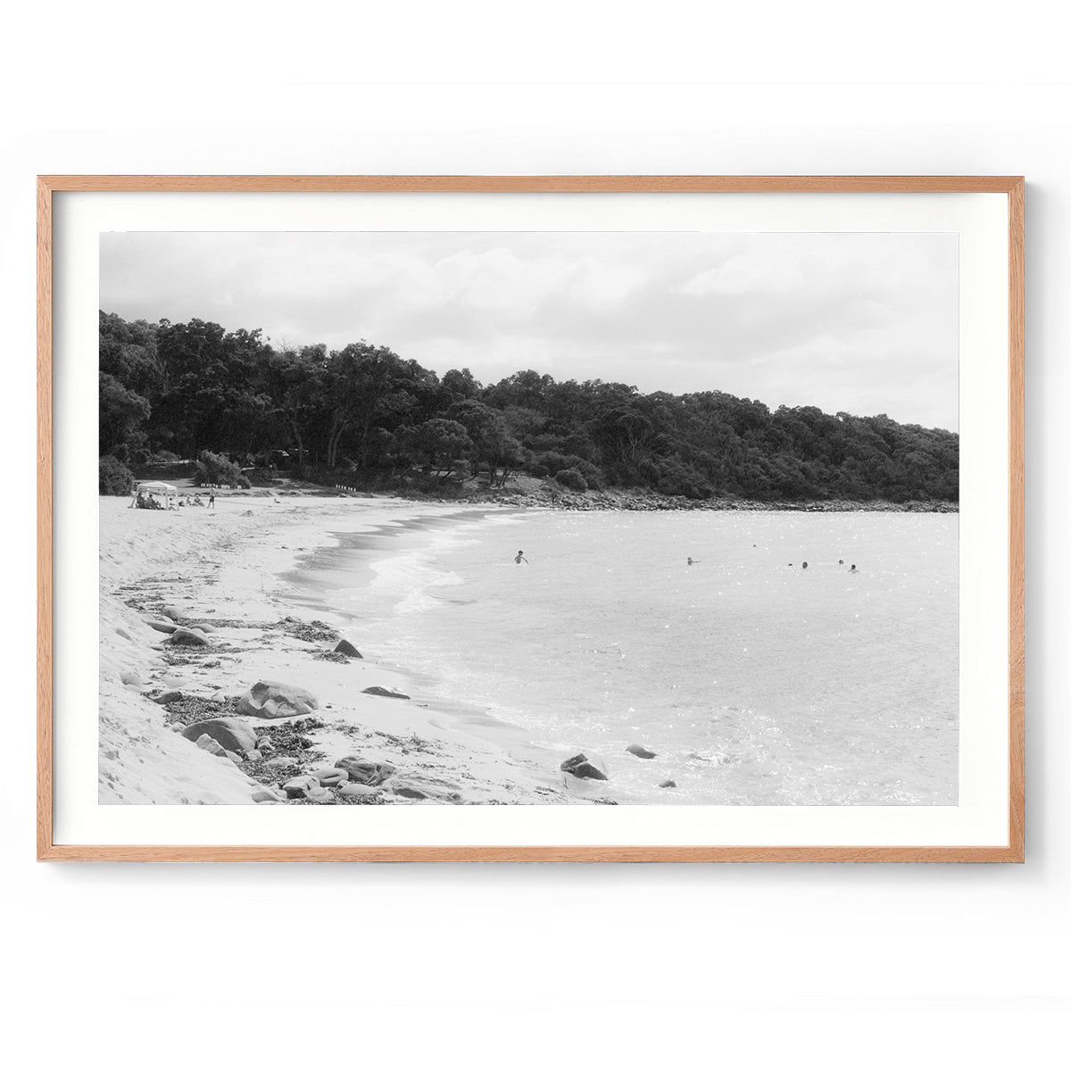 Black and white photo of Meelup beach in Western Australia's south west with people in the ocean and the bush wrapping around the coastline. Shot on film with a nostalgic, vintage feel. Available framed in black, white or oak.