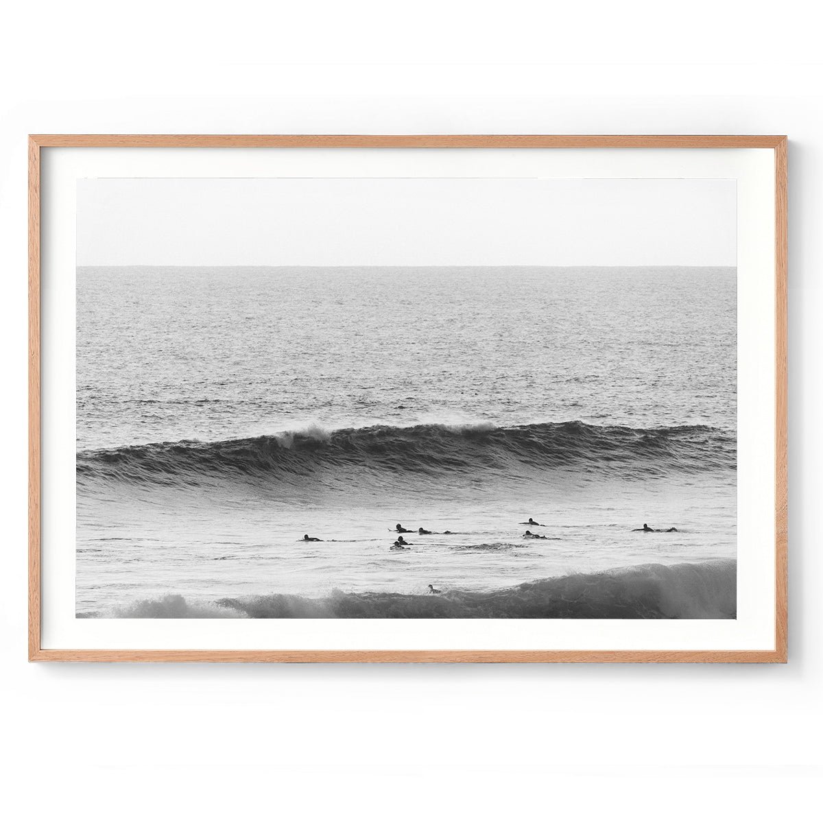 Minimalist black and white photo of surfers paddling out towards a wave in the ocean at Yallingup Beach, Western Australia. Fine art photography prints, available framed in black, white or oak.