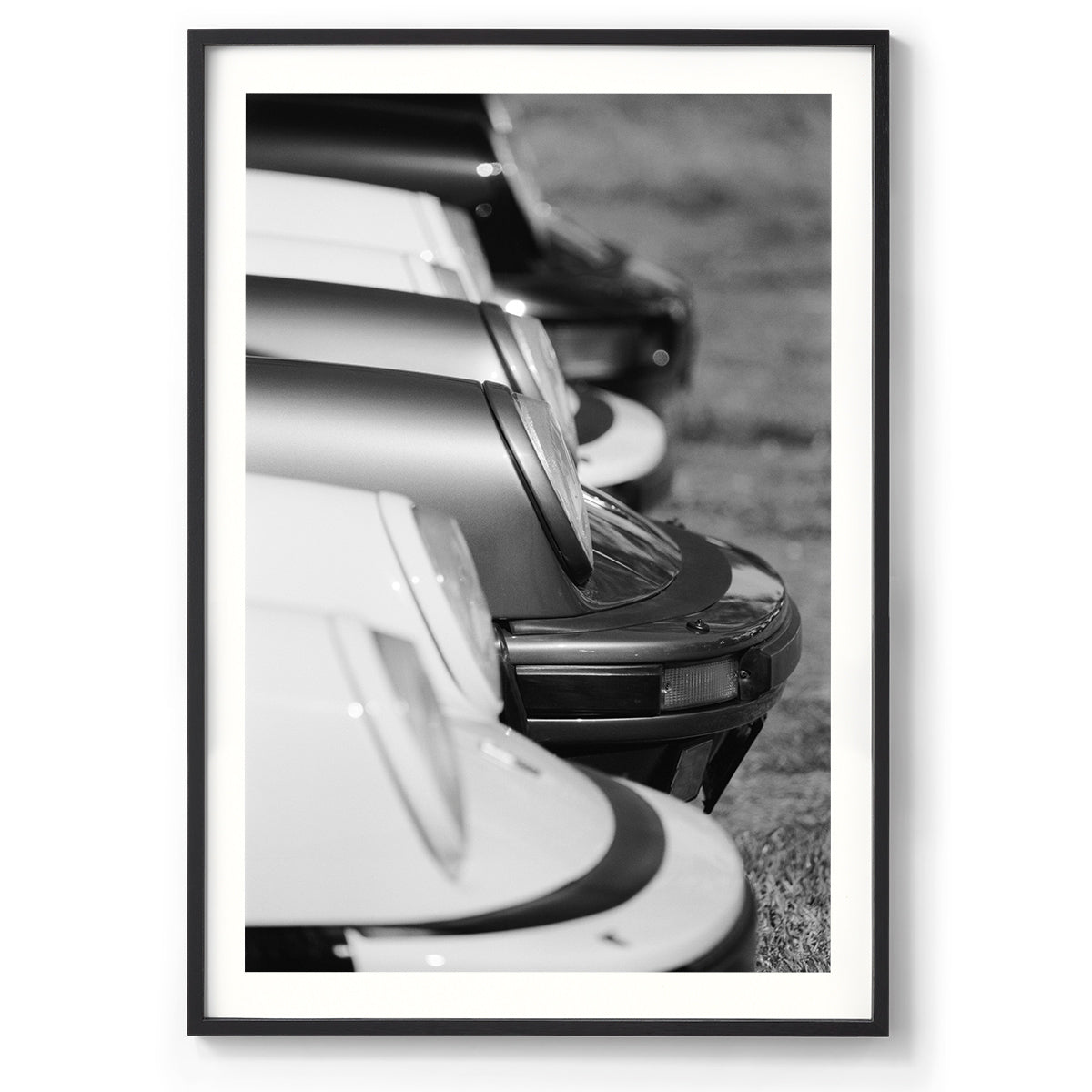 Vertical black and white photo of the front of multiple Porsche 911s from the side all lined up showing just the iconic round headlights and bumpers. Fine art photography prints, available framed in black, white and oak.