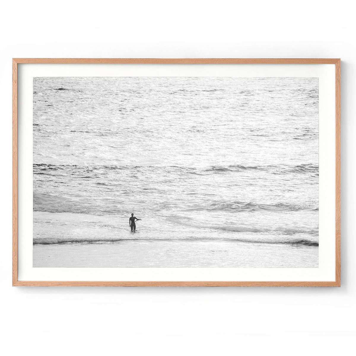 Black and white photo of a female surfer holding a surf board on her hip looking out whilst standing in the ocean at Yallingup Beach. Fine art photography prints, available framed in black, white or oak.