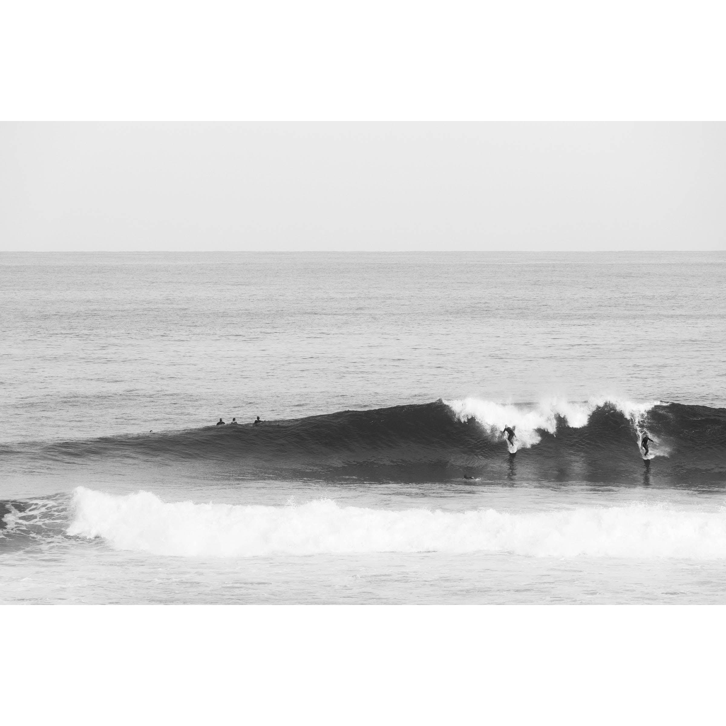 Black and white photo of two surfers riding a wave in the ocean at Surfer's Point, Margaret River, Western Australia. Fine art photography print, available framed in black, white or oak.