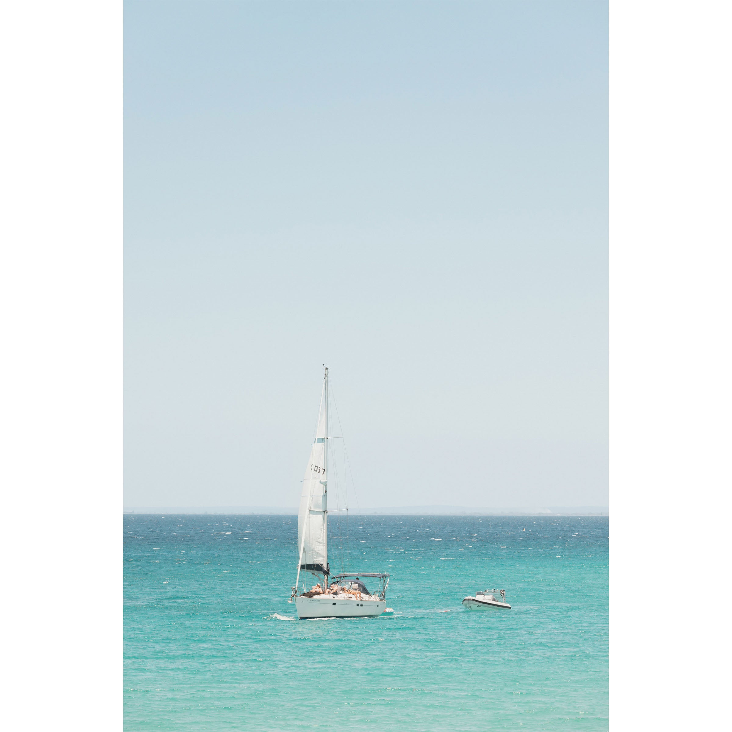 Colour photo of a sailboat on the water off Eagle Bay in Western Australia, tugging a smaller boat. There are people sunbathing on the deck. Fine art photography print, available framed in black, white or oak.