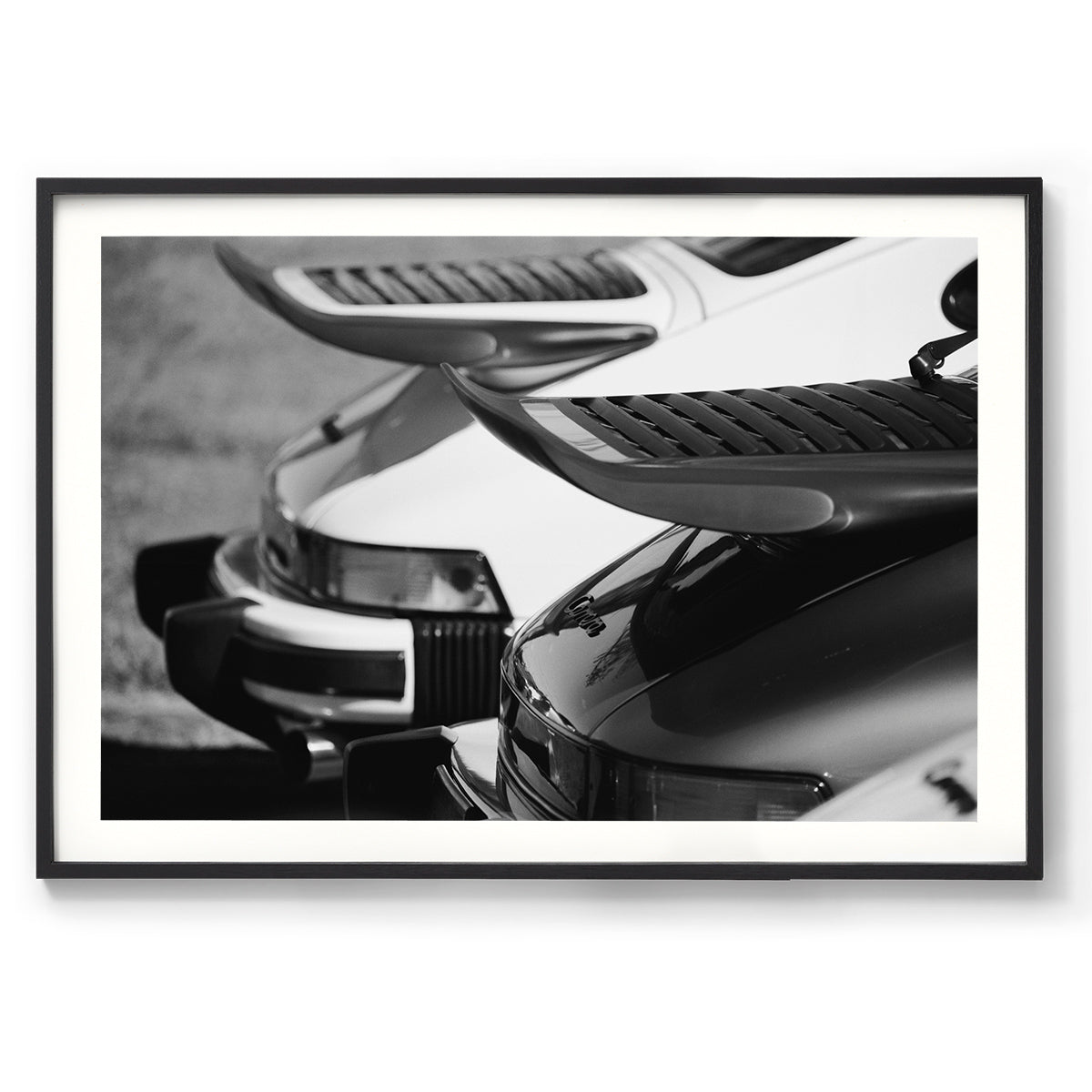 Black and white photo of the back of two Porsche 911s showing the iconic whale tail spoilers. Fine art photography prints, available framed in black, white or oak.