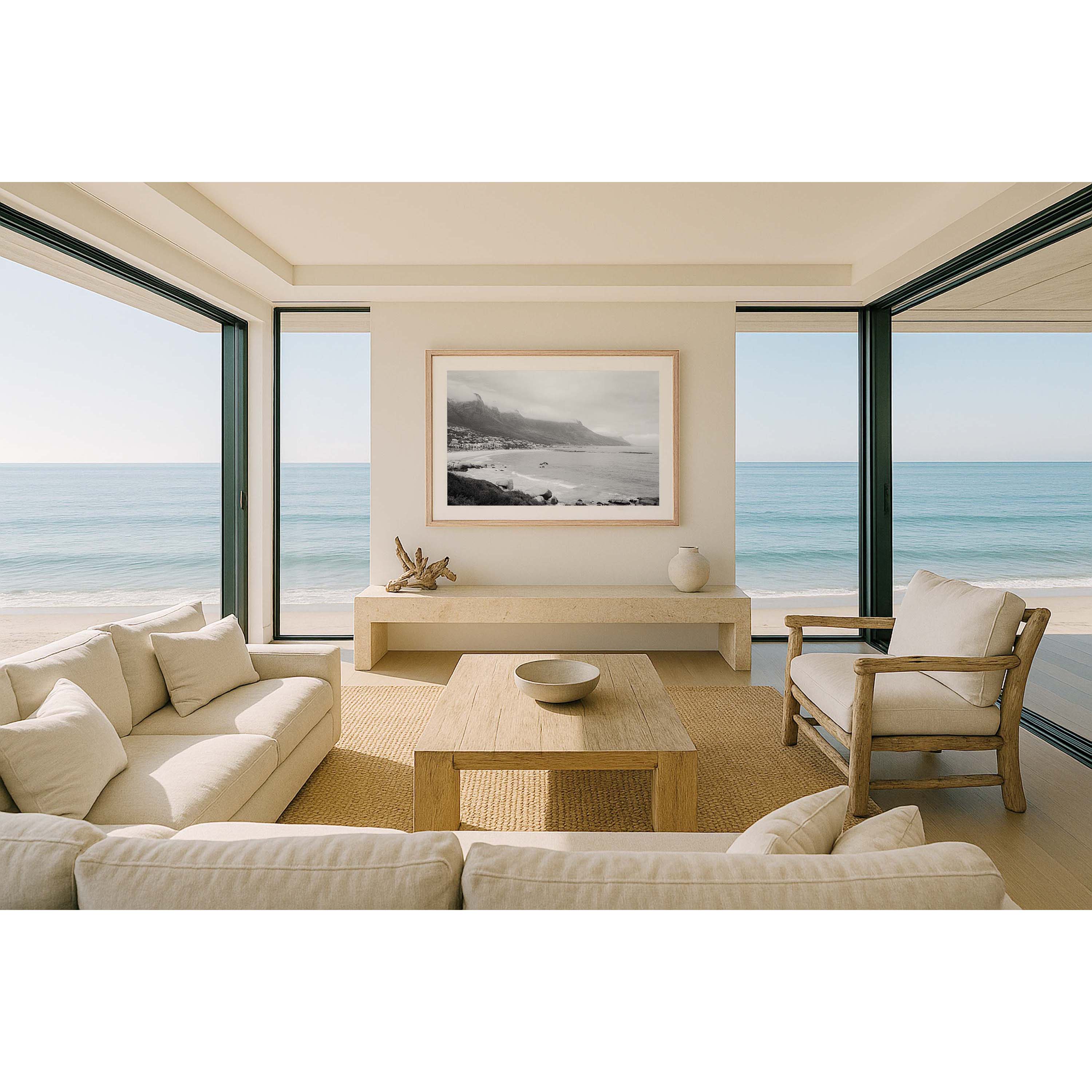 Framed black and white photo of Camps Bay in Cape Town, South Africa. Shot on film on a moody day, the clouds are covering the tops of the mountains and gentle waves roll in as the city curves around the beach. Available framed in black, white or oak.