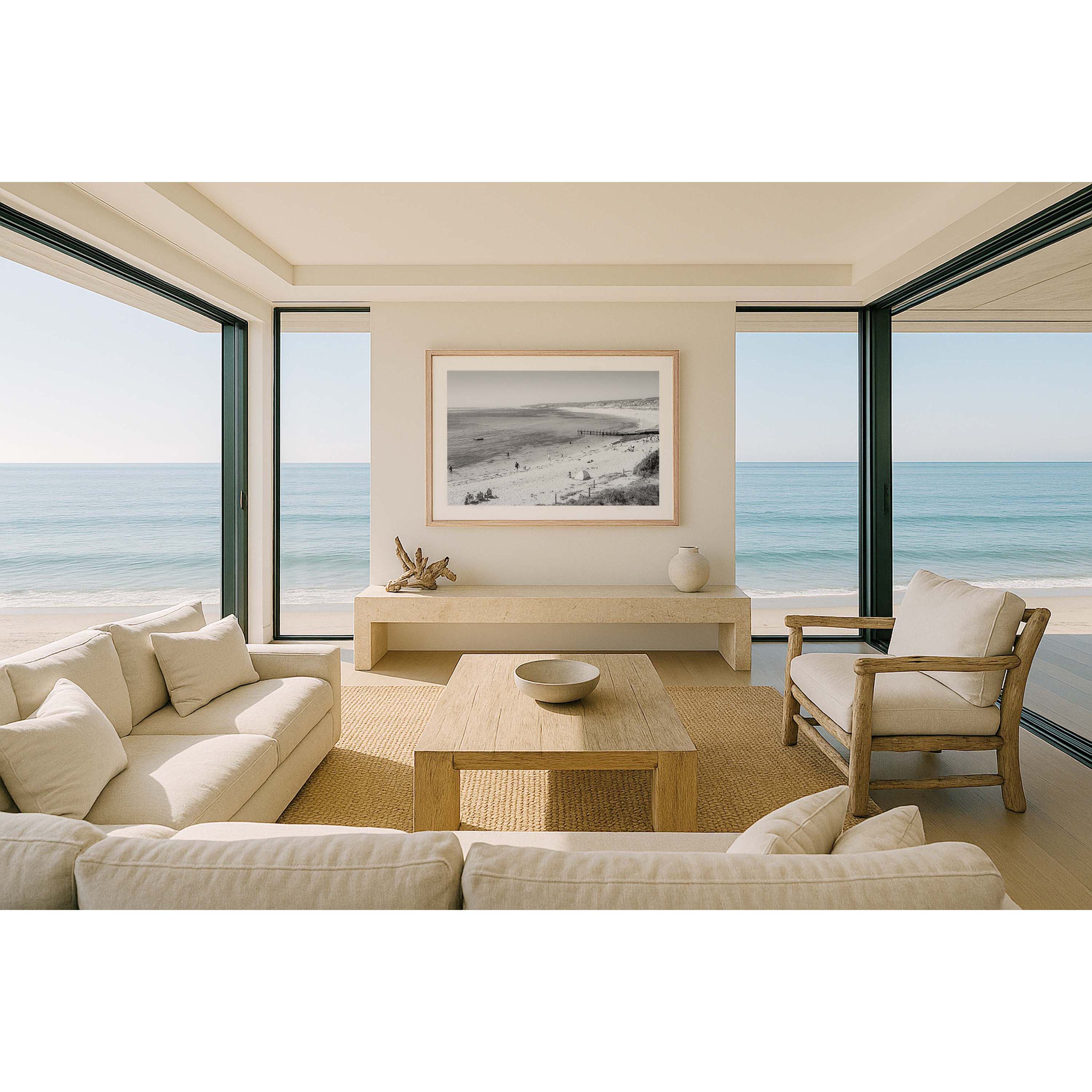 Black and white photo of Gnarabup Beach in Margaret River, Western Australia. It's a sunny day and there are people on the sand and in the water, a tent on the beach and the jetty sits out in front of the beach curving around under the cliffs. Available framed in black, white or oak.